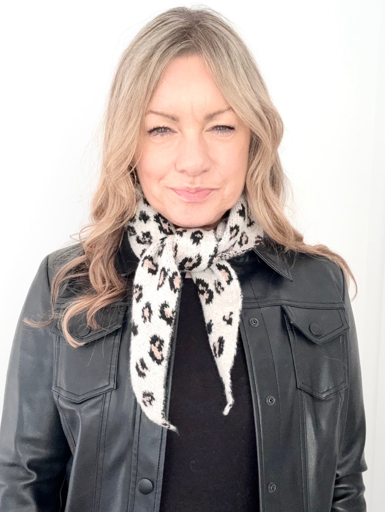 Woman wearing a black leather jacket and a cream animal print knitted scarf with black leopard print 