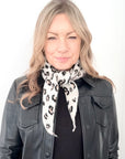 Woman wearing a black leather jacket and a cream animal print knitted scarf with black leopard print 