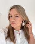 Woman wearing a white shirt with a cream, brown and gold beaded disk earring. 