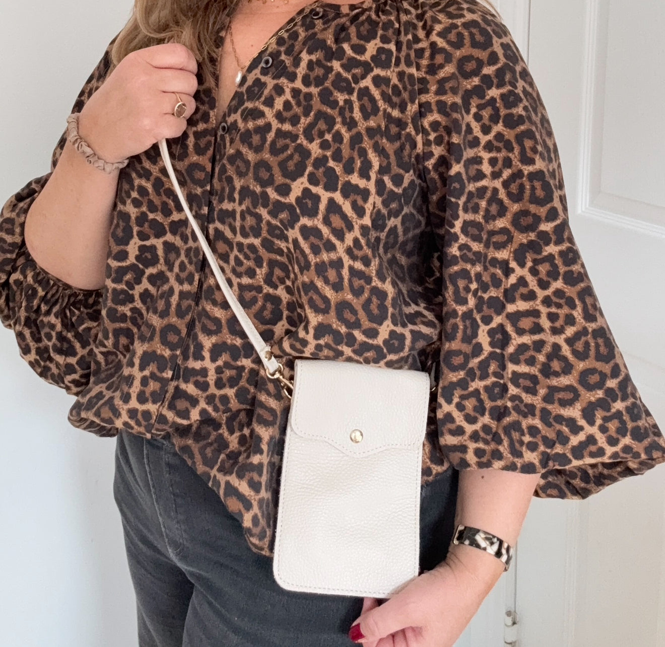woman wearing a leopard print top holding a white crossbody phone bag