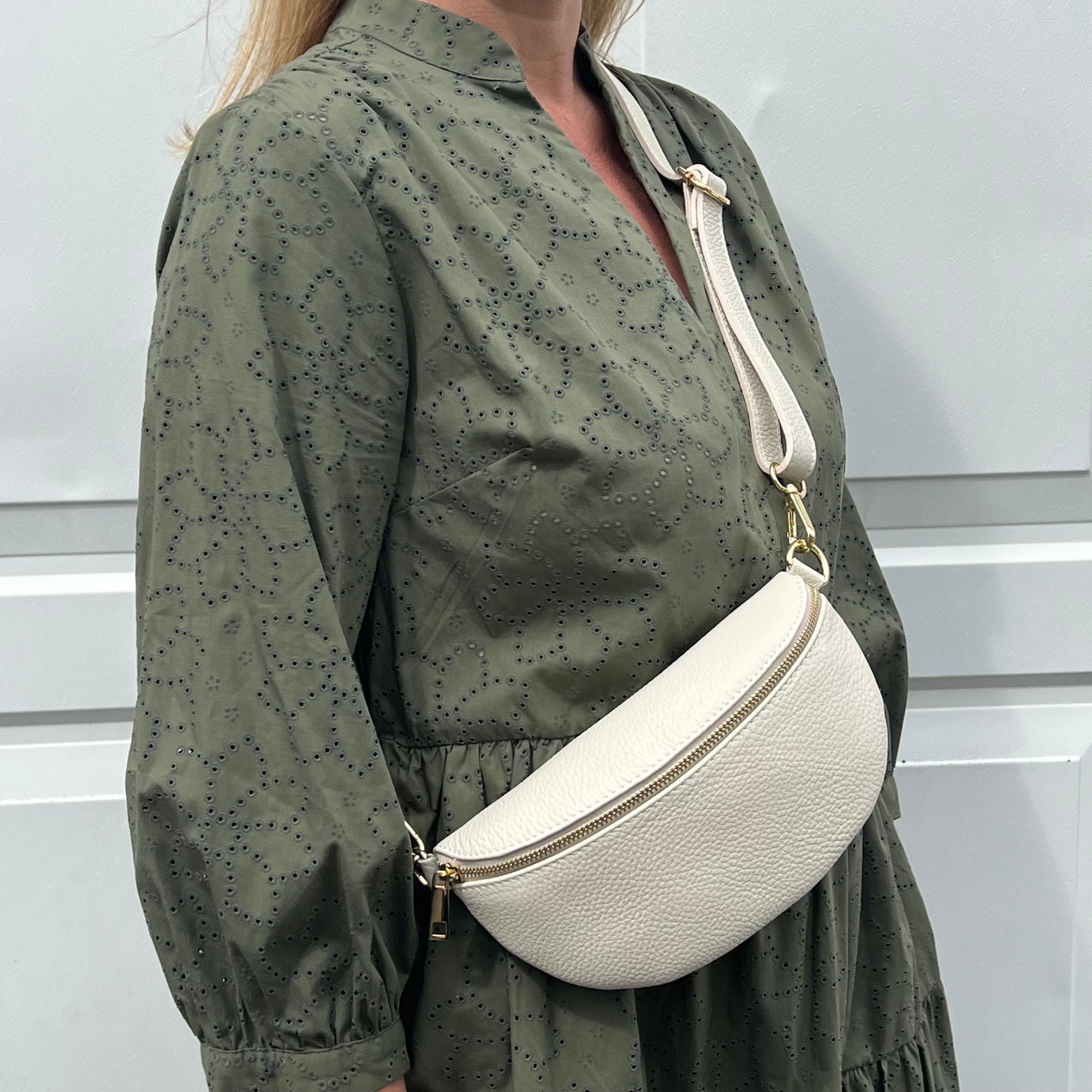 A woman wearing a green dress with a cream leather crossbody bag with an adjustable strap.