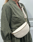 A woman wearing a green dress with a cream leather crossbody bag with an adjustable strap.