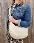 Woman wearing a denim jacket and leopard print dress holding a cream crossbody handbag.
