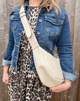 Woman wearing a denim jacket and leopard print dress holding a cream crossbody handbag.