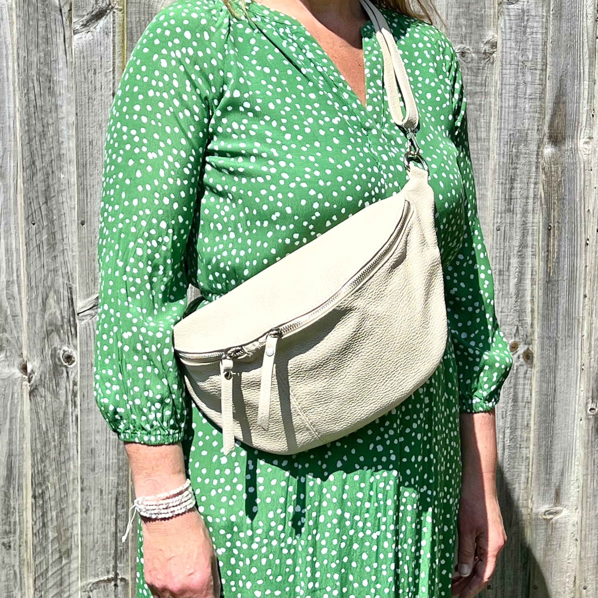 A person wearing a cream-colored large crossbody bum bag with an adjustable, detachable leather strap and multiple zip pockets, carried over the shoulder.
