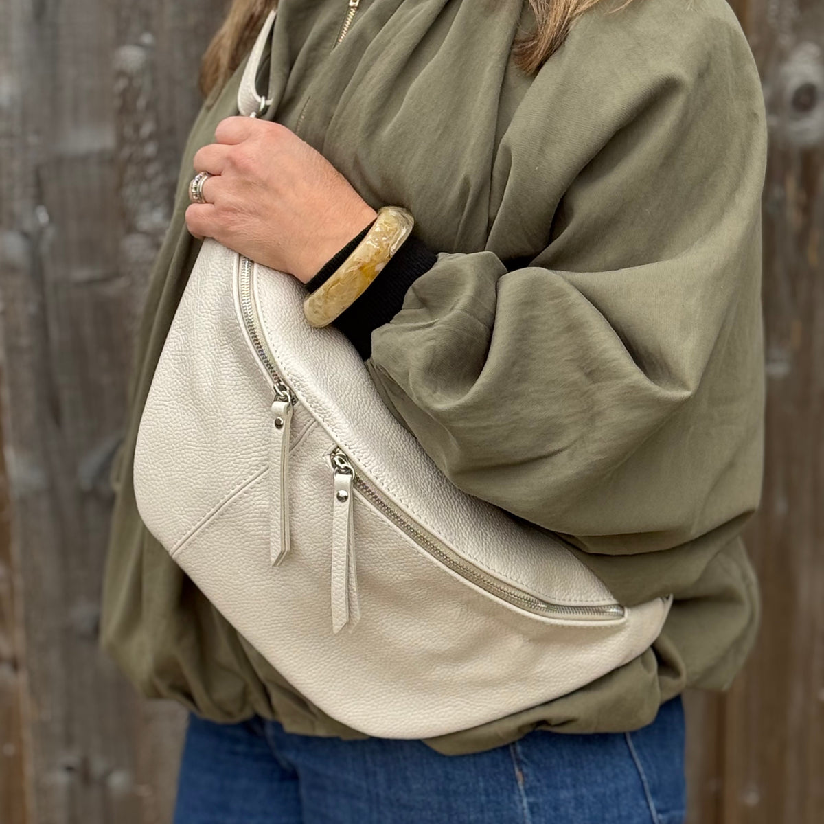 Woman wearing a green shirt with a large cream crossbody bum bag.