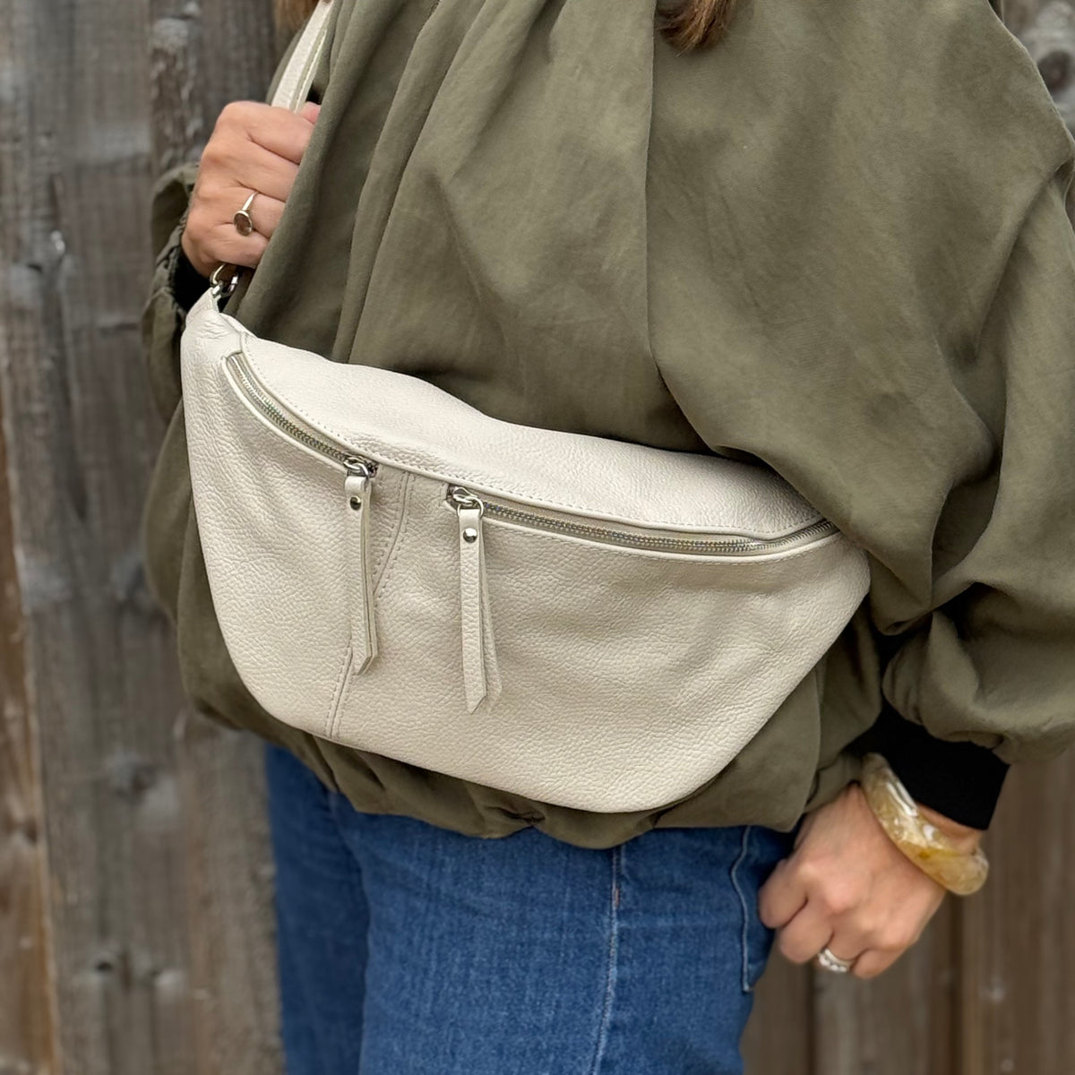 Woman wearing a green shirt with a large cream crossbody bag with a wooden background.