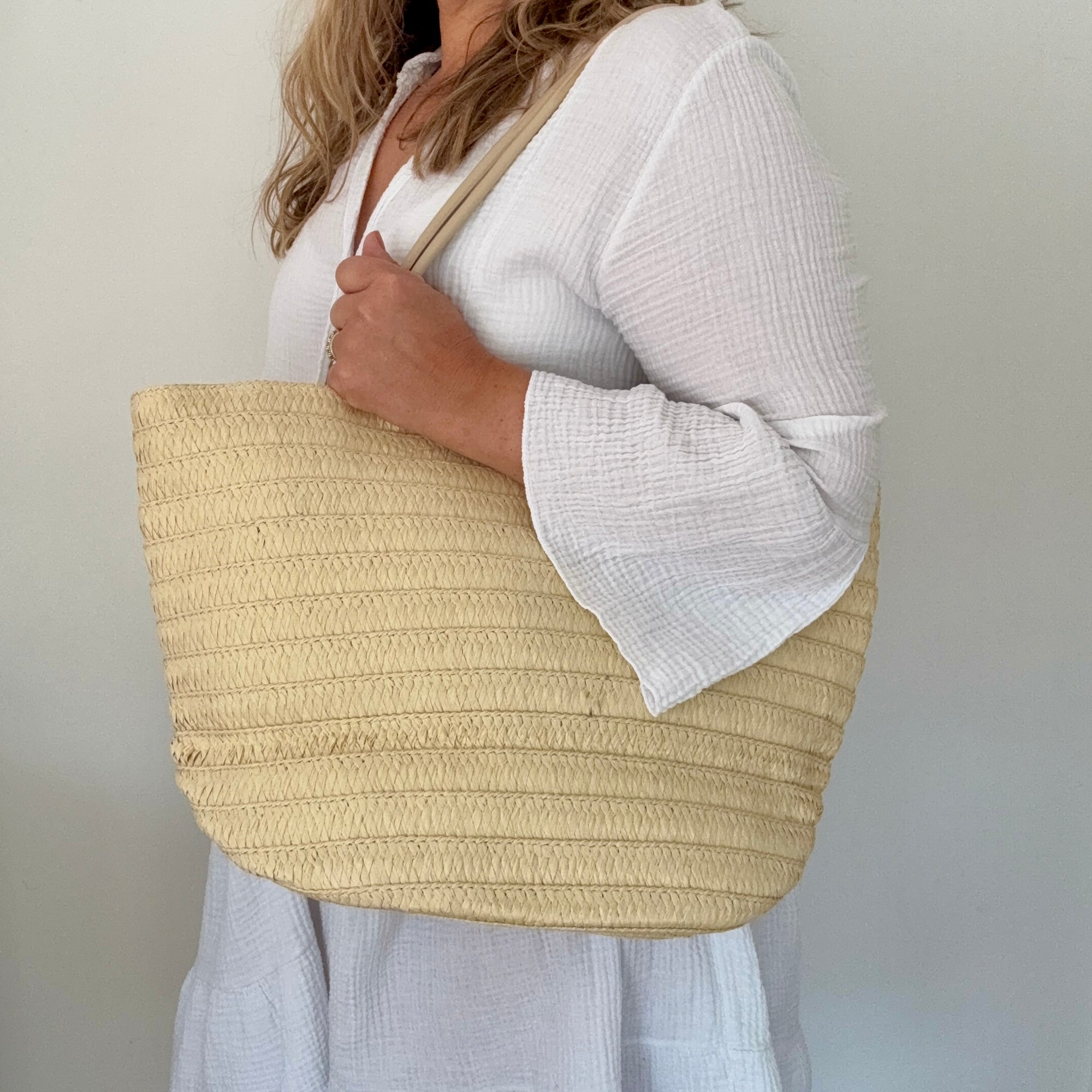 woman holding a beige woven tote bag against a plain background