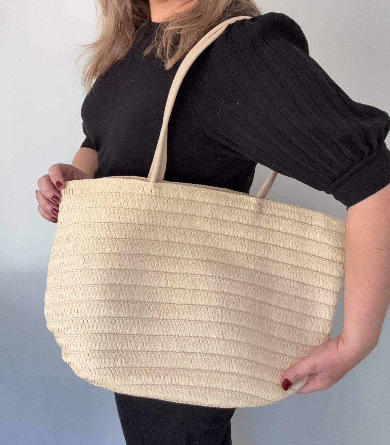 A person holding a cream-colored raffia tote bag with a PU handle strap.