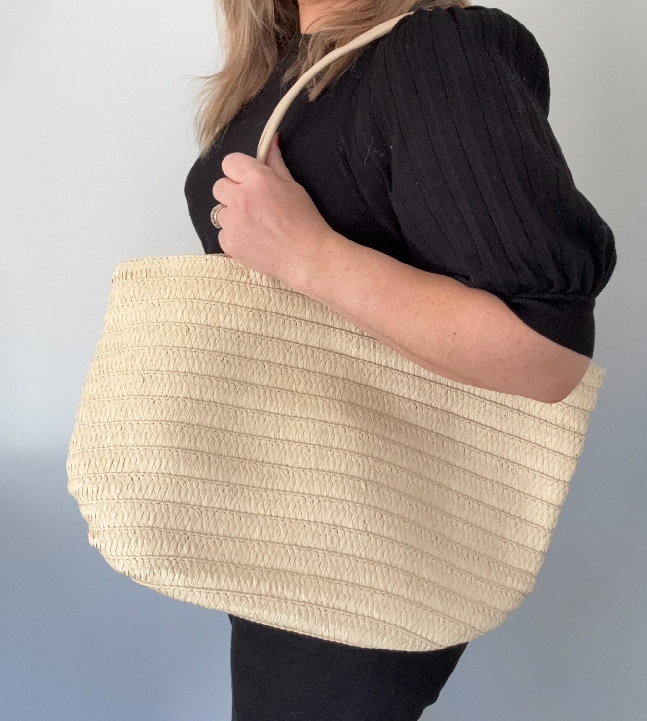 A person holding a cream-colored raffia tote bag with a PU handle strap.