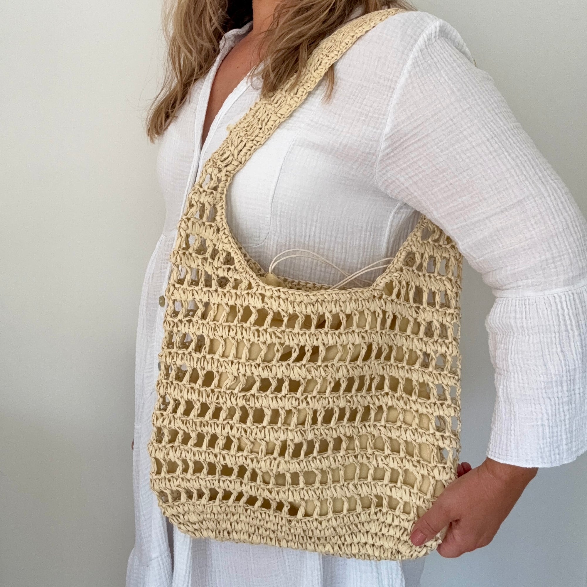 Person wearing a cream crochet bag over their shoulder against a plain background