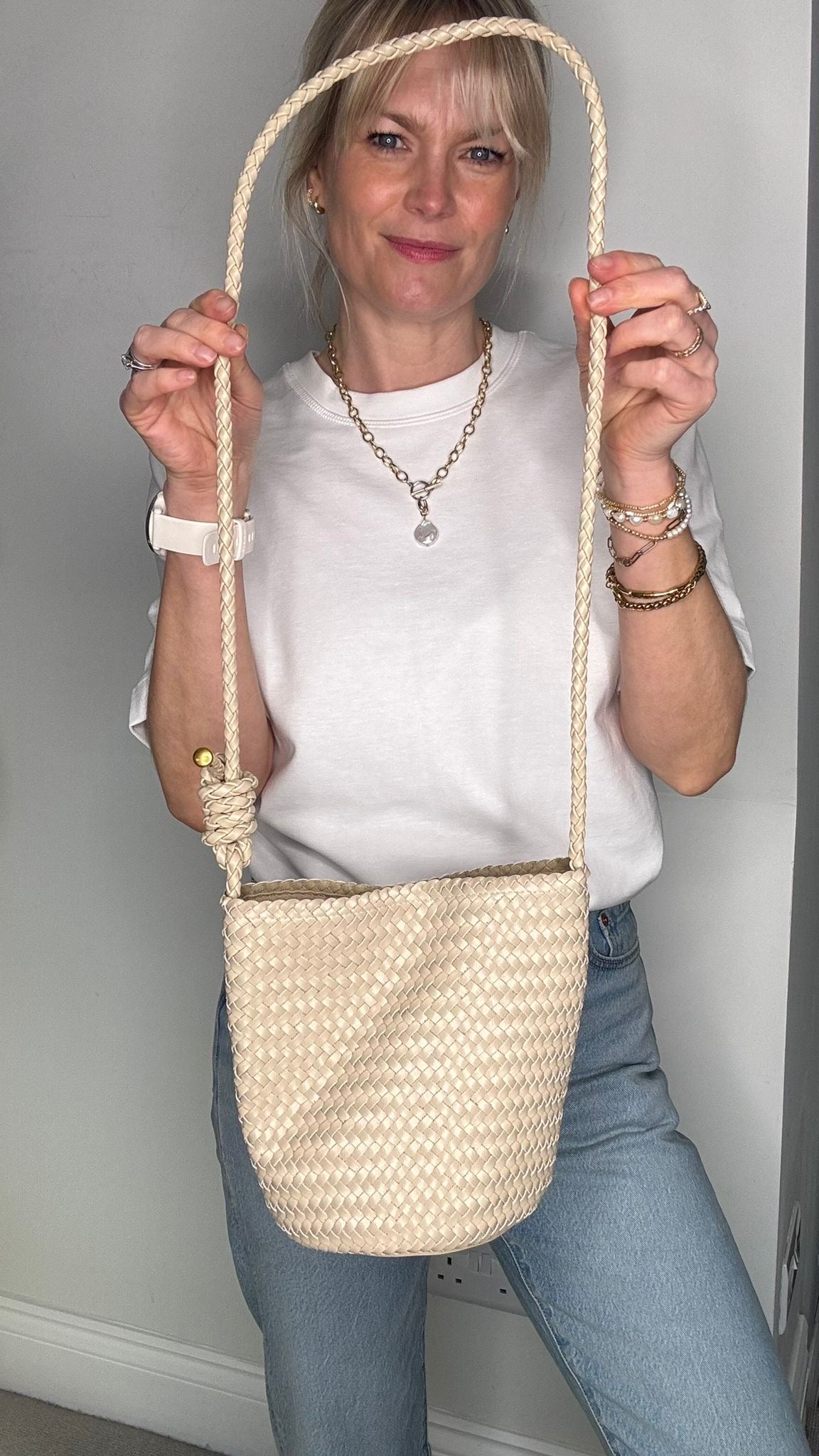 Woman wearing a white shirt and wearing a cream woven crossbody handbag.