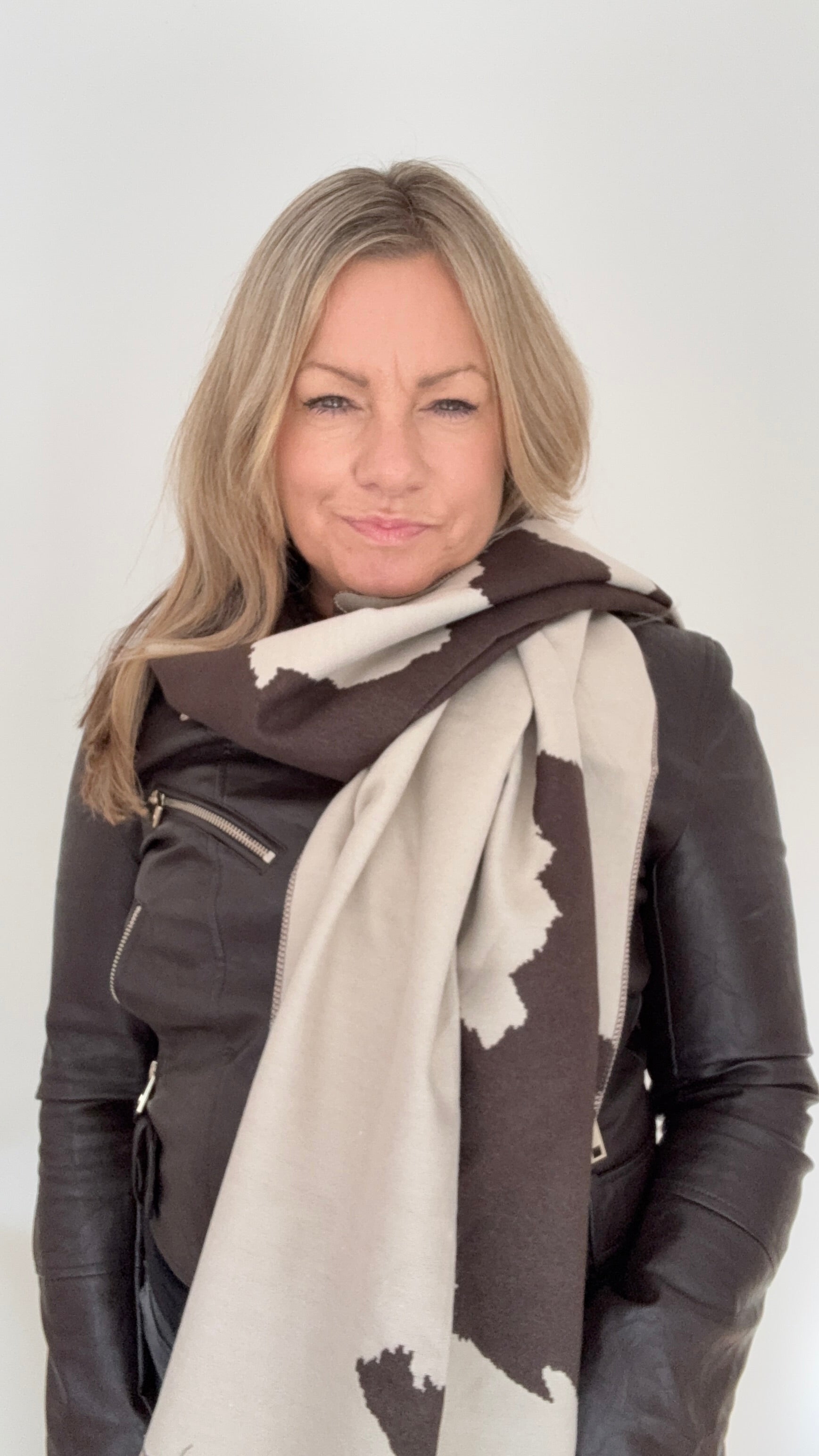 Woman wearing a brown leather jacket and a large scarf with a  Dark Brown & Cream Cow print pattern for Autumn Winter