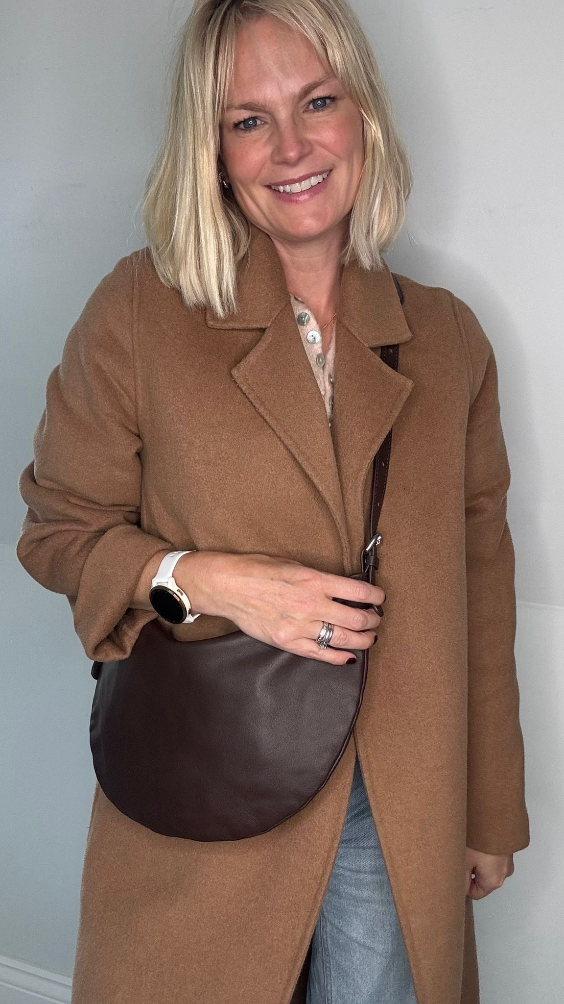 Woman wearing a brown coat holding a dark brown crossbody/ shoulder leather bag 