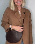 Woman wearing a brown coat holding a dark brown crossbody/ shoulder leather bag 