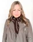 Woman wearing a grey leather jacket and a dark brown and dark taupe stripe knitted scarf 