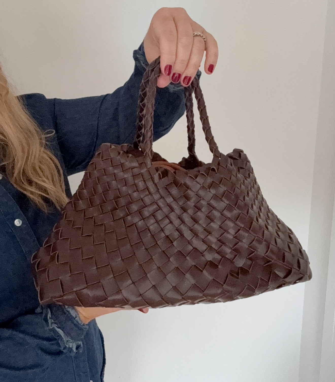 Brown woven handbag held by a person against a white background