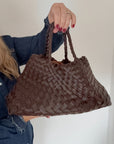 Brown woven handbag held by a person against a white background