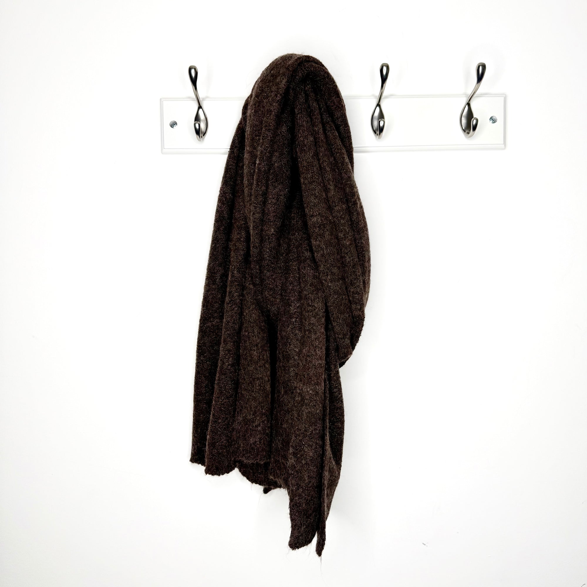 Brown knitted scarf hanging on a hook against a  white wall 