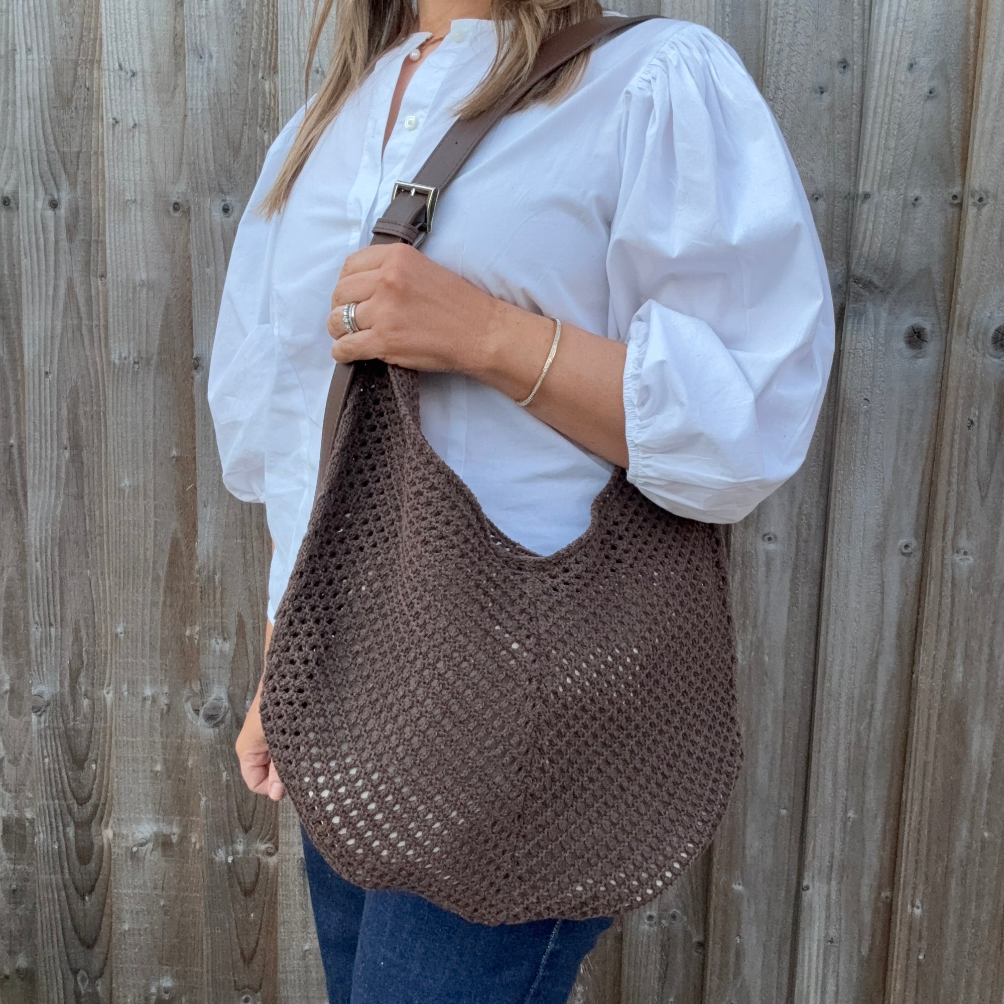 Woman wearing a white shirt and holding a brown woven crossbody handbag. 