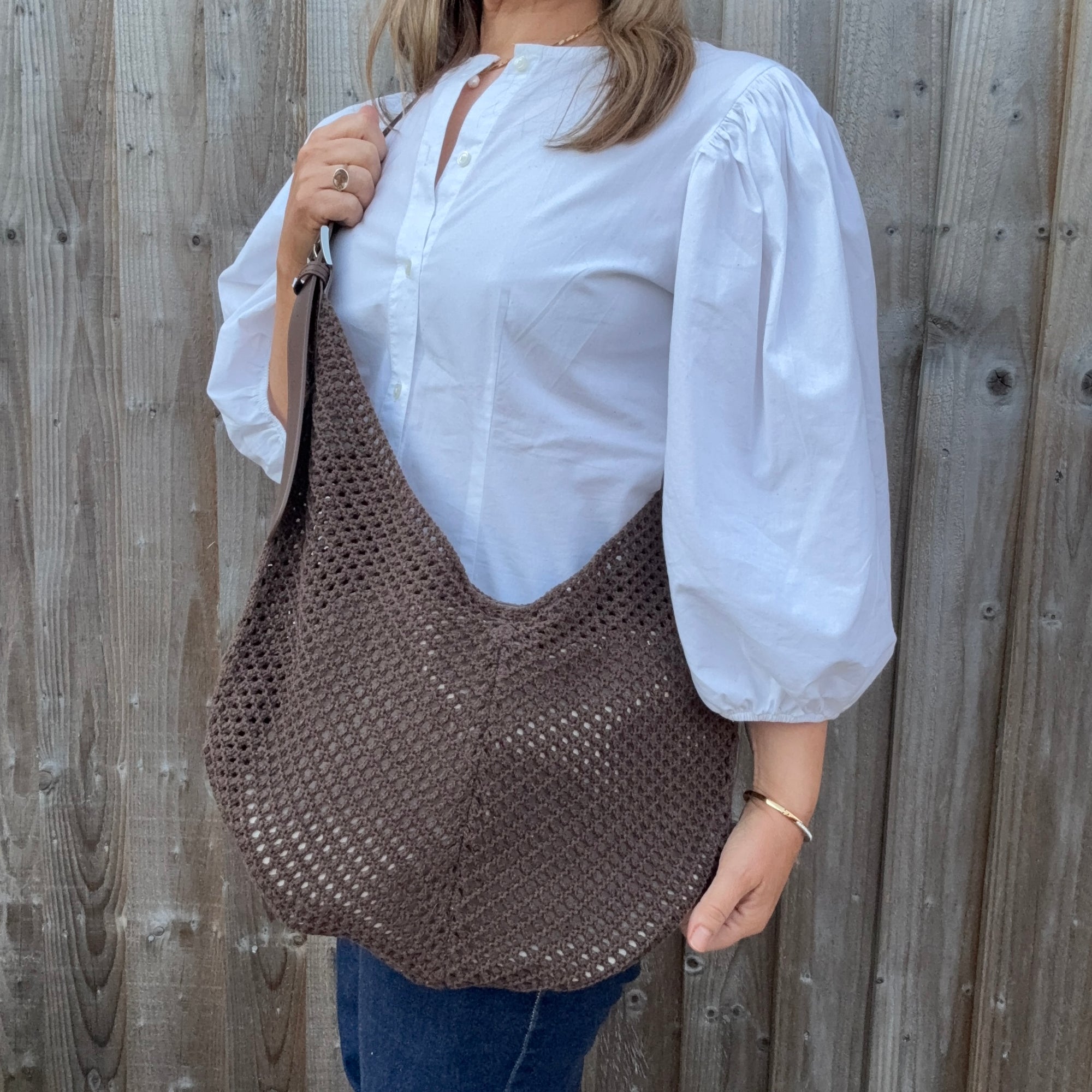 Woman wearing a white shirt and holding a brown woven crossbody handbag. 