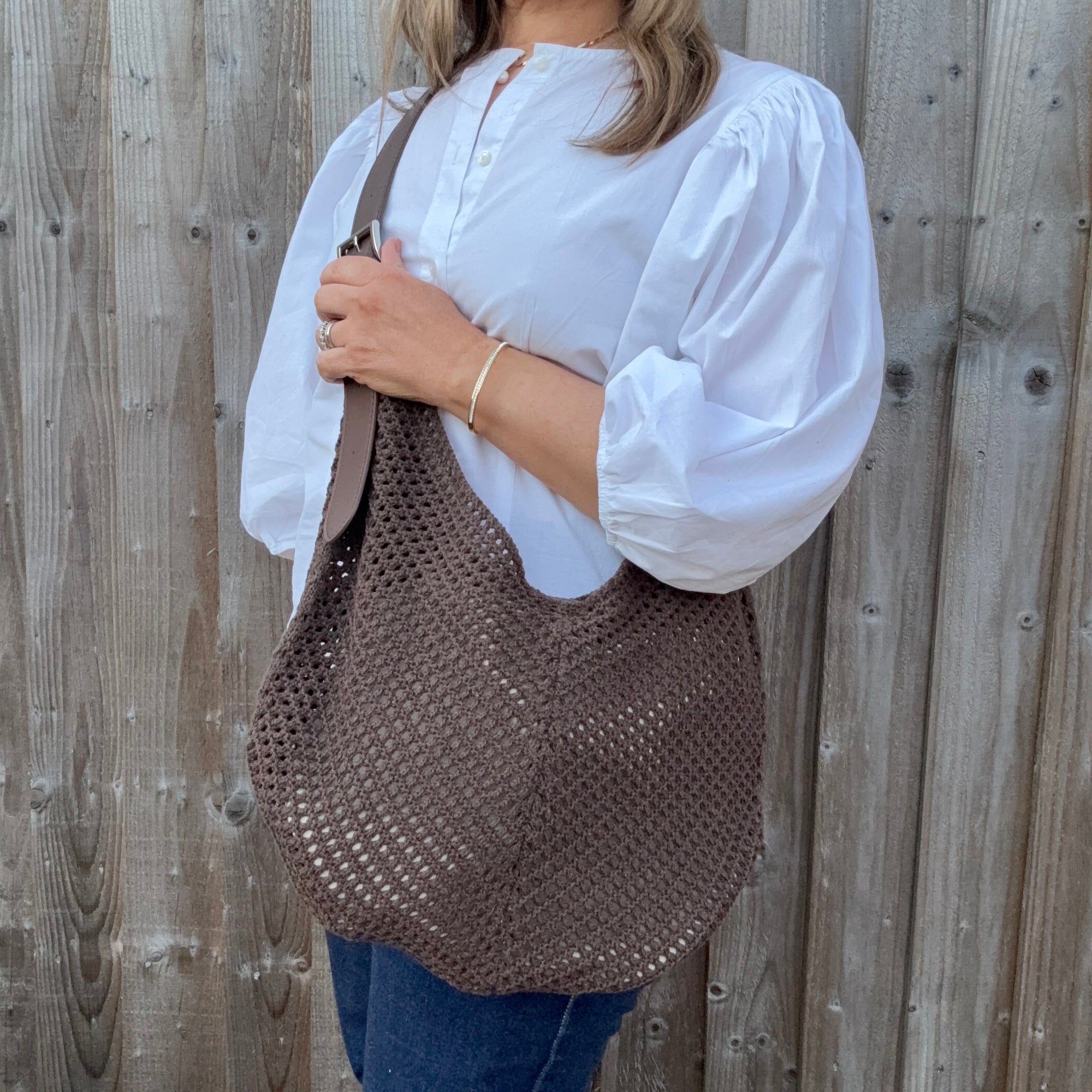 Woman wearing a white shirt and holding a brown woven crossbody handbag. 