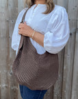 Woman wearing a white shirt and holding a brown woven crossbody handbag. 