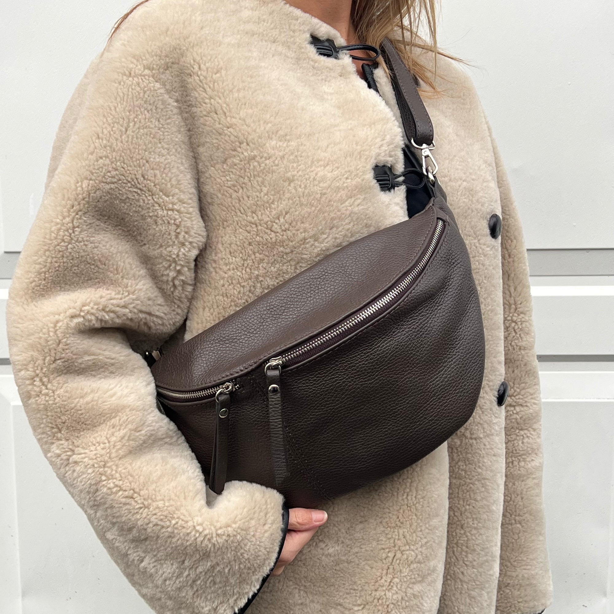 woman wearing a dark brown large crossbody bum bag with gold accented hardware. 