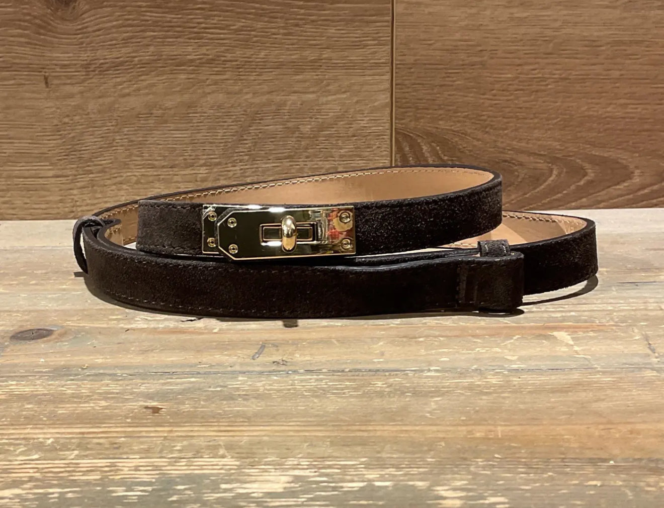 Dark brown narrow leather belt with gold buckle on a wooden background