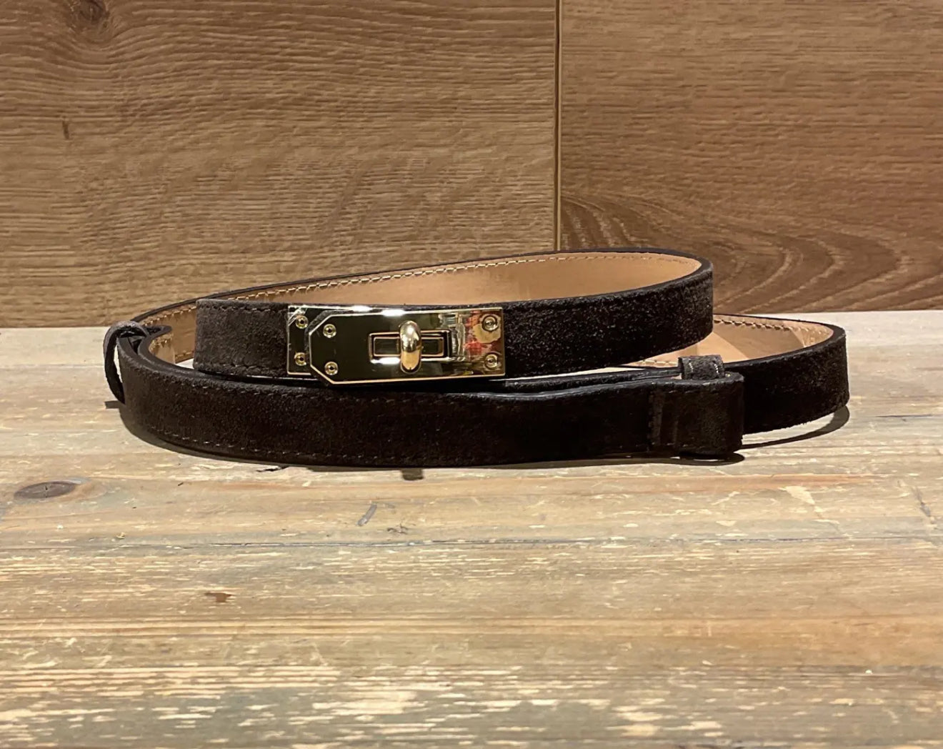 dark brown narrow suede leather belt with a gold buckle on a wooden surface