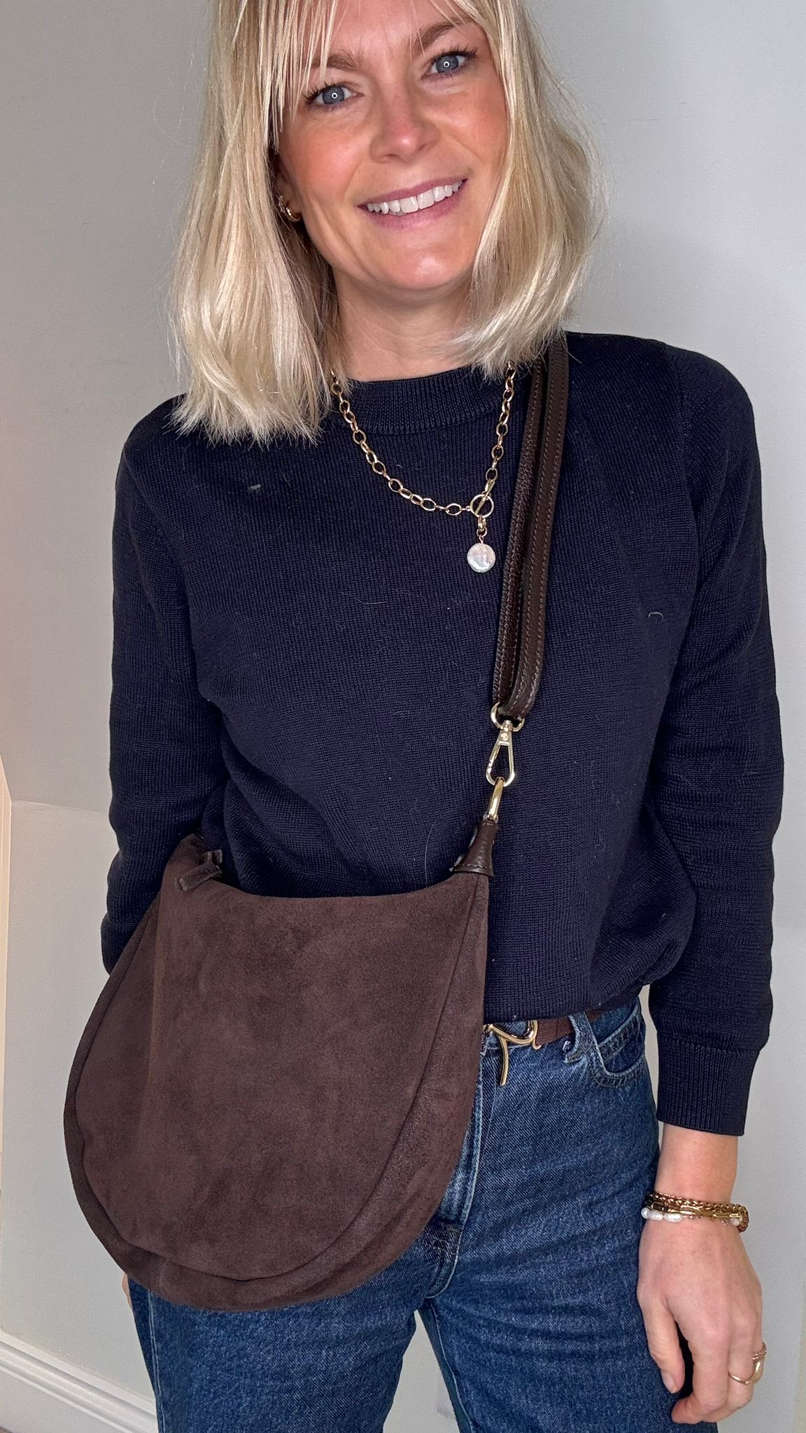 Woman holding a dark brown suede crossbody / shoulder bag 