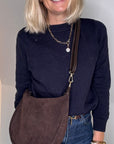 Woman holding a dark brown suede crossbody / shoulder bag 