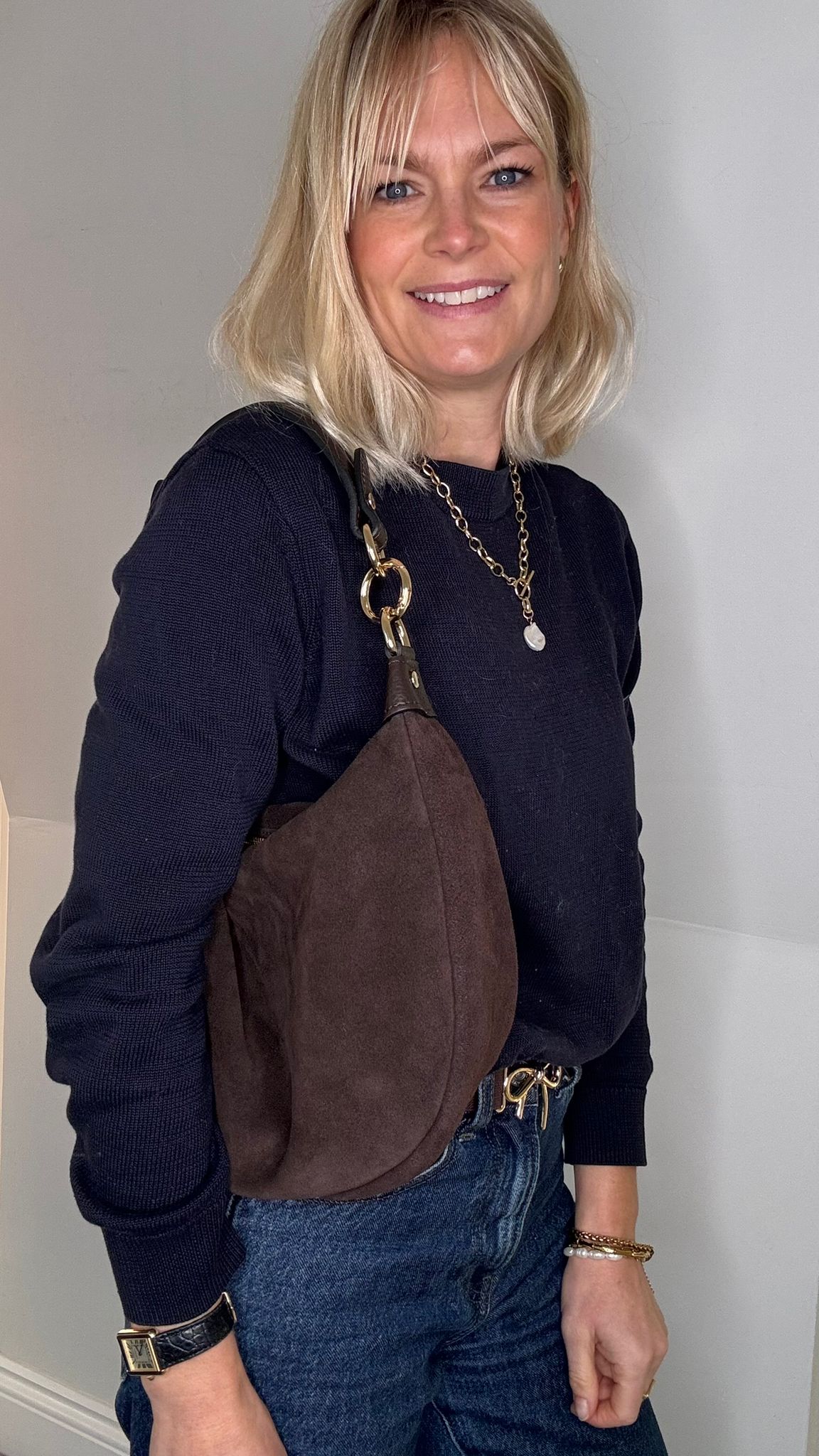 Woman wearing a navy sweater and dark brown suede crossbody / shoulder bag 