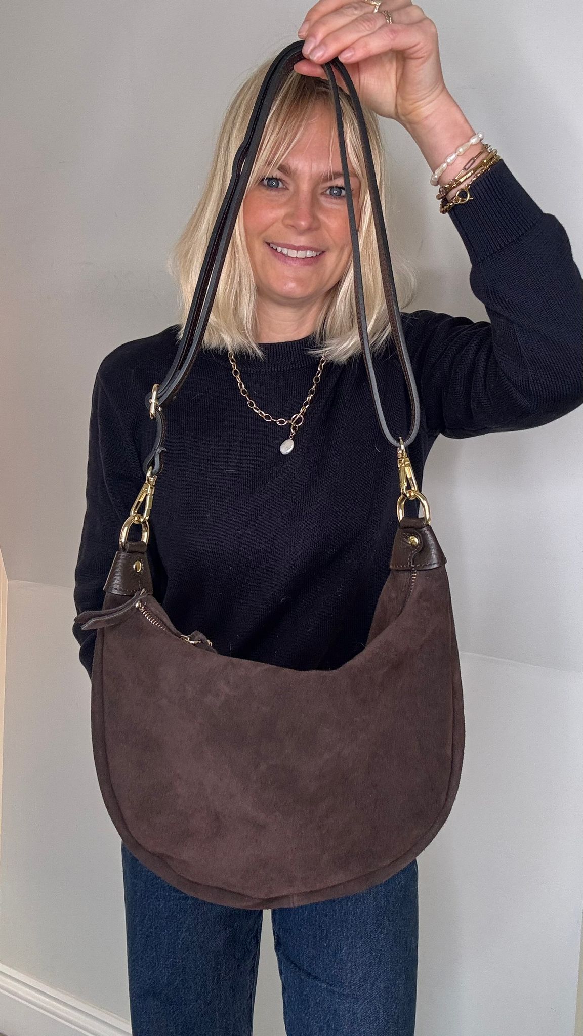woman holding a dark brown suede crossbody / shoulder handbag with a plain background
