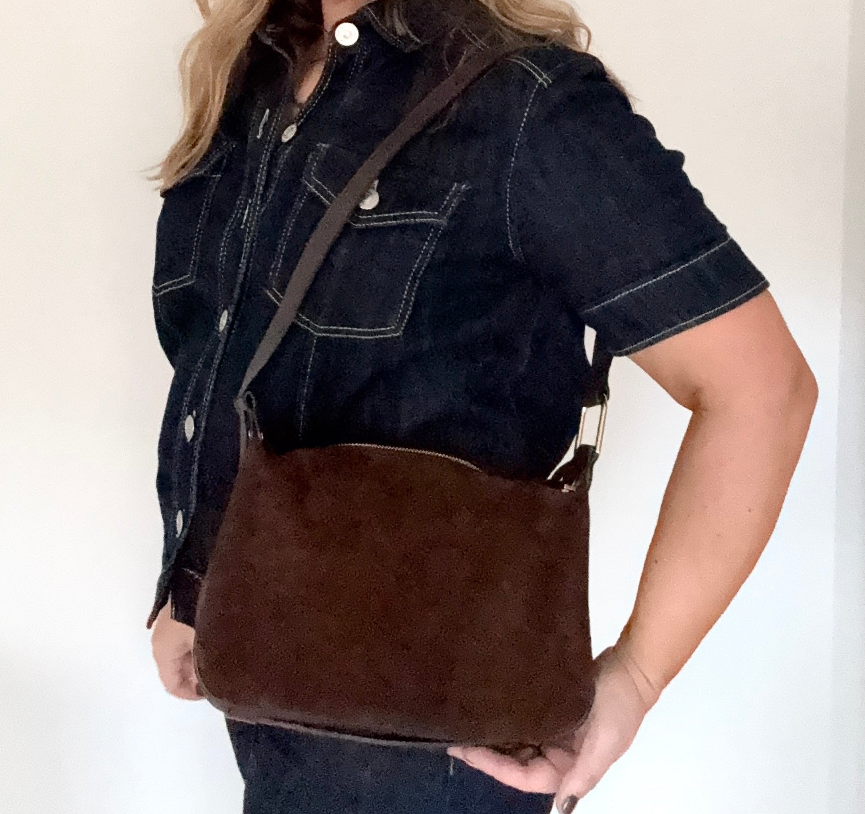 woman wearing a dark denim jacket holding a dark brown suede and leather crossbody/ shoulder bag 