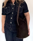 woman wearing a dark denim outfit holding a dark brown suede and leather tote / shoulder bag with a brown shoulder strap