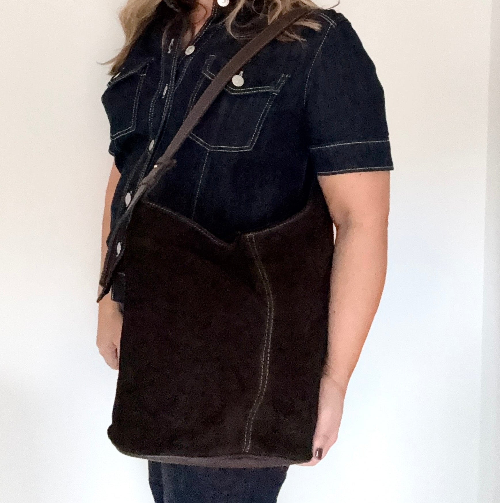woman wearing a dark denim jacket with a dark brown suede and leather tote/ shoulder bag over their shoulder 