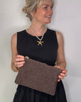 Woman wearing a black dress, holding a dark brown clutch / crossbody handbag. 