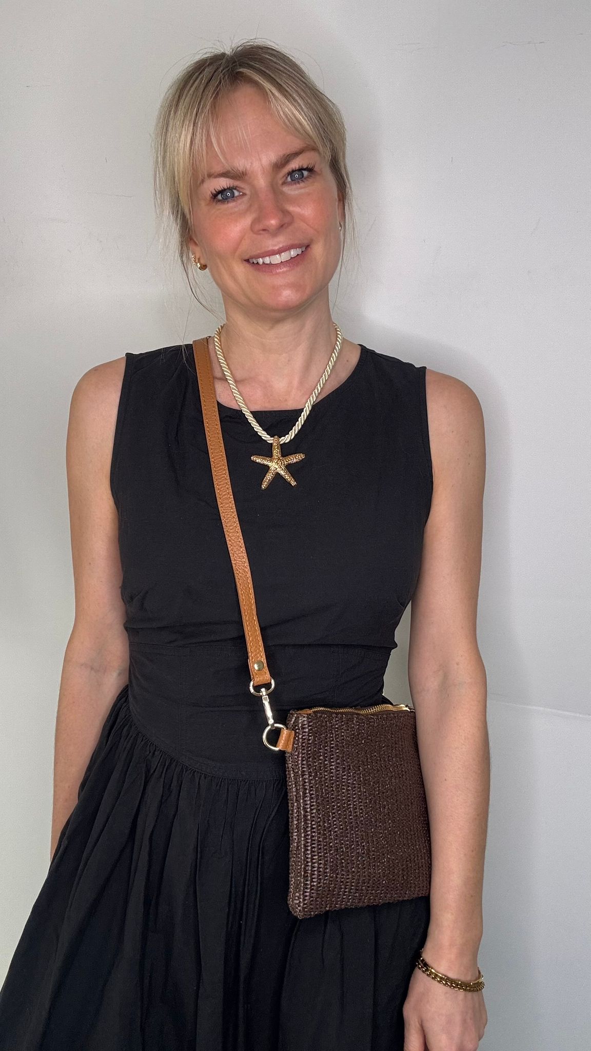 Woman wearing a black dress, holding a dark brown clutch / crossbody handbag. 