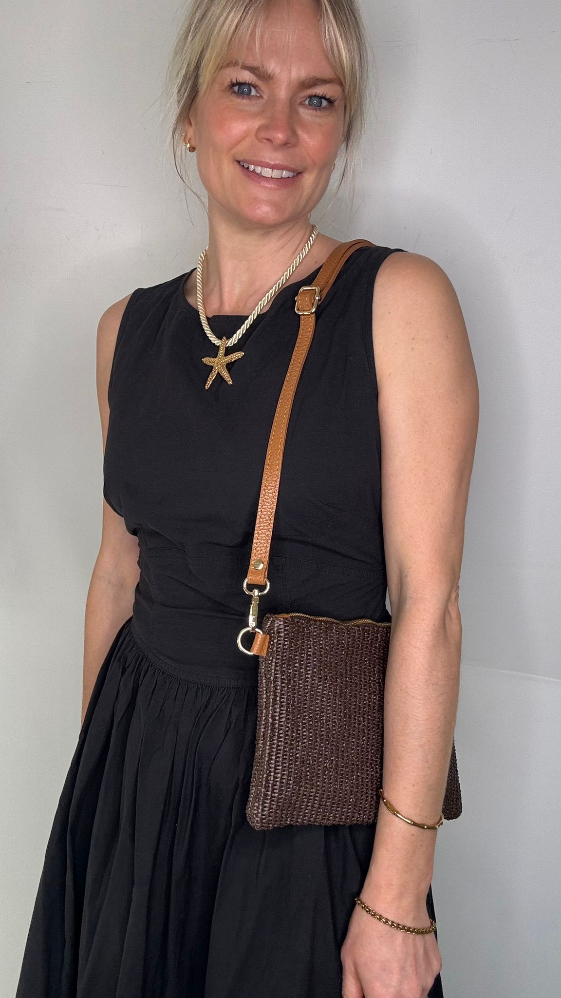 Woman wearing a black dress, holding a dark brown clutch / crossbody handbag. 
