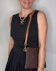 Woman wearing a black dress, holding a dark brown clutch / crossbody handbag. 