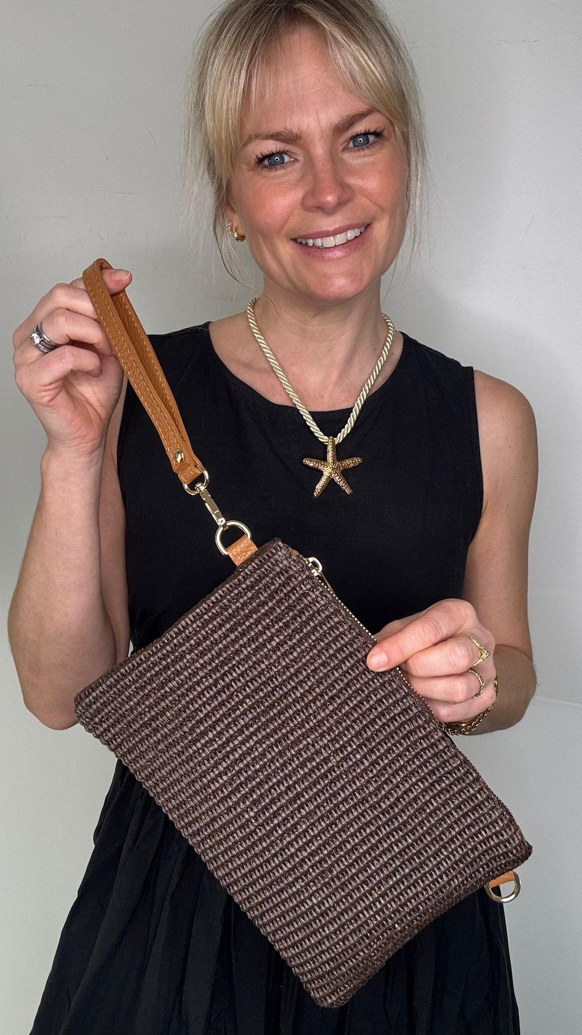 Woman wearing a black dress, holding a dark brown clutch / crossbody handbag. 