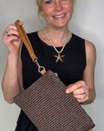 Woman wearing a black dress, holding a dark brown clutch / crossbody handbag. 