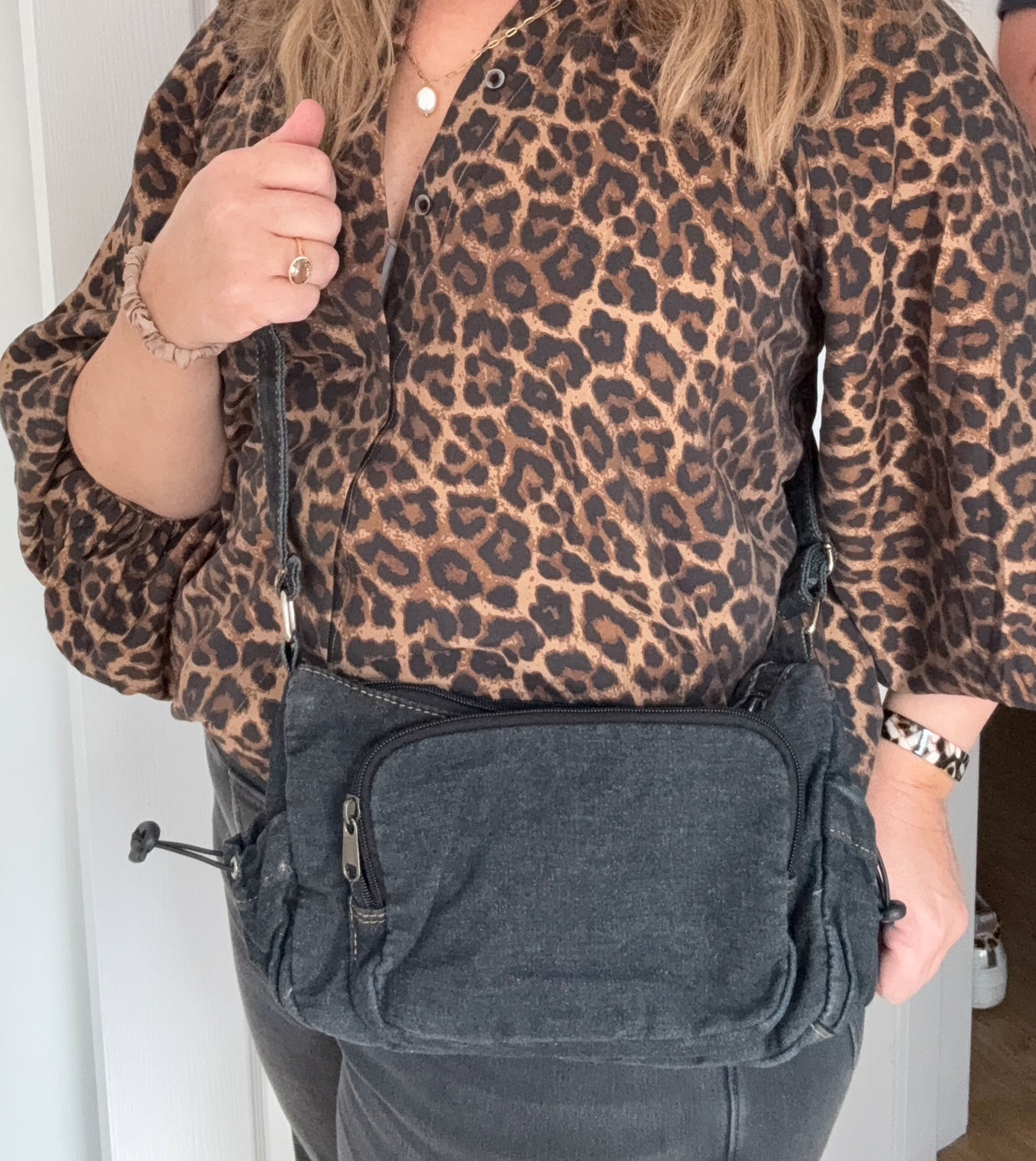 woman wearing a leopard print top with a dark grey denim crossbody bag.