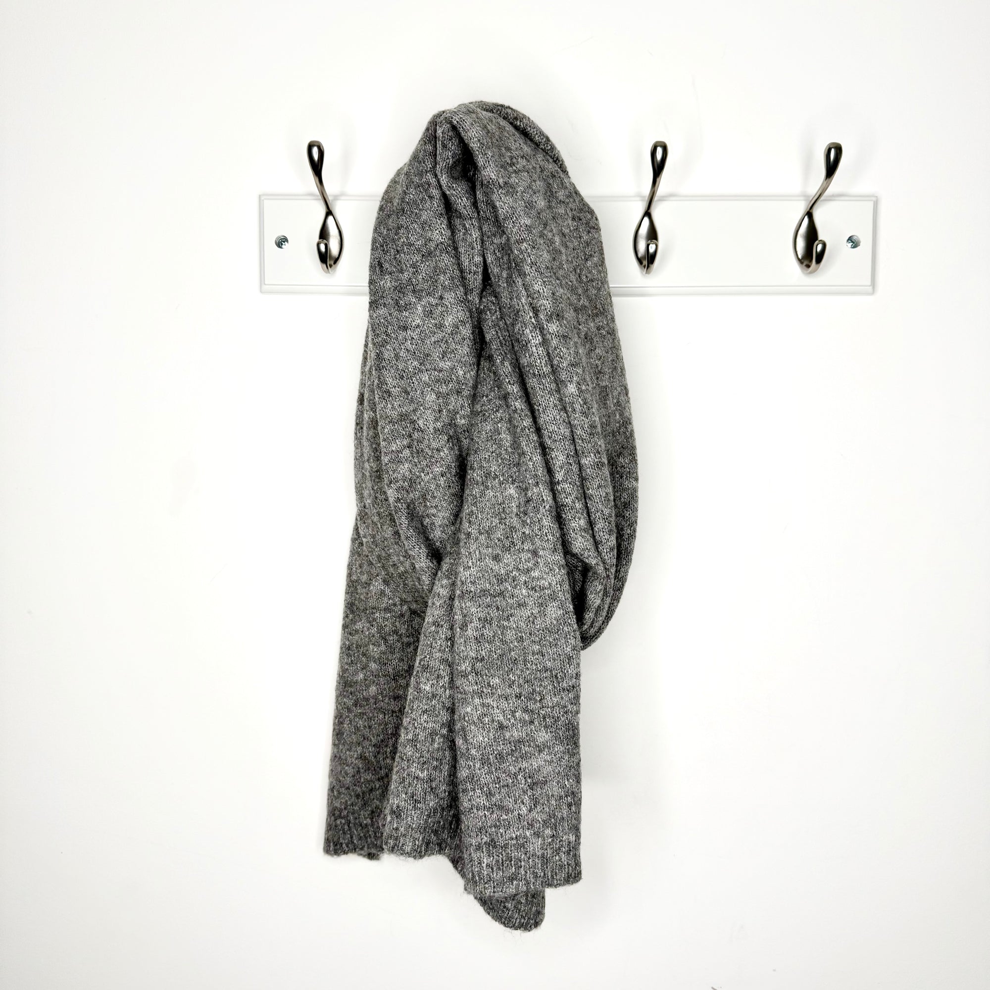 dark grey scarf draped over a peg against a white wall 