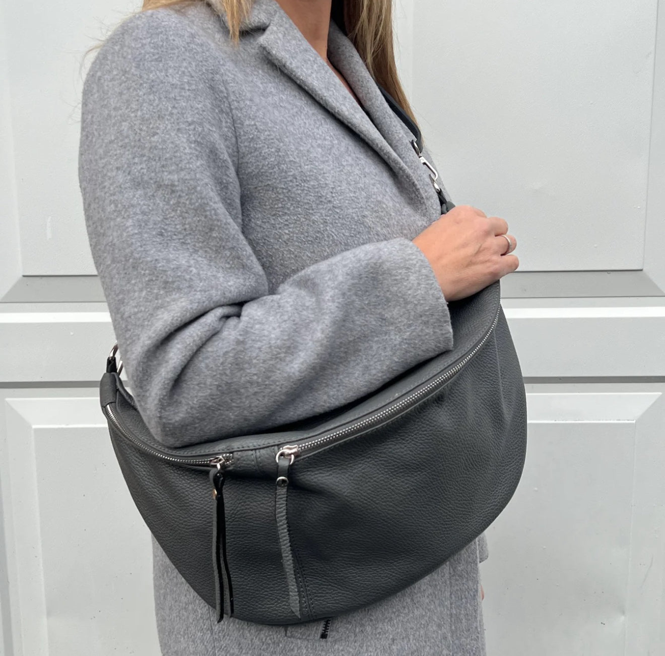 Lady wearing a grey coat holding a dark grey XL Crossbody handbag.
