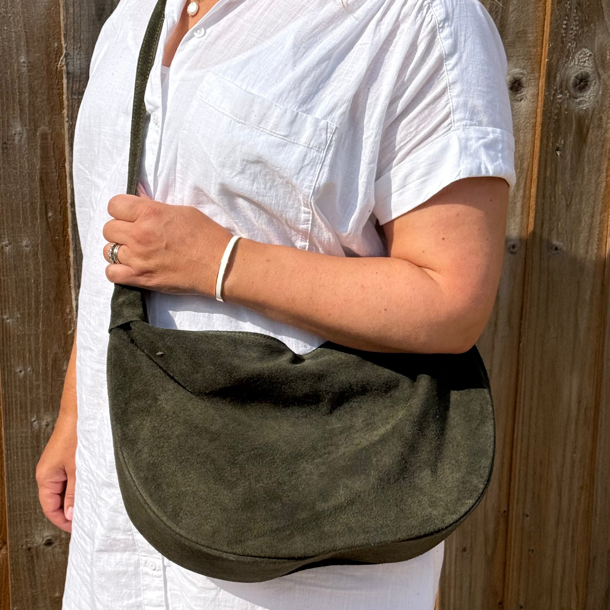 woman wearing a white shirt holding a dark khaki suede large crossbody bag 