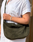 woman wearing a white shirt holding a dark khaki suede large crossbody bag 