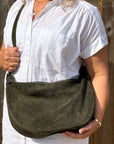 woman wearing a white shirt holding an dark khaki suede crossbody bag