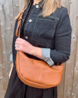 Woman wearing a denim jacket and black dress, holding a dark tan crossbody handbag.